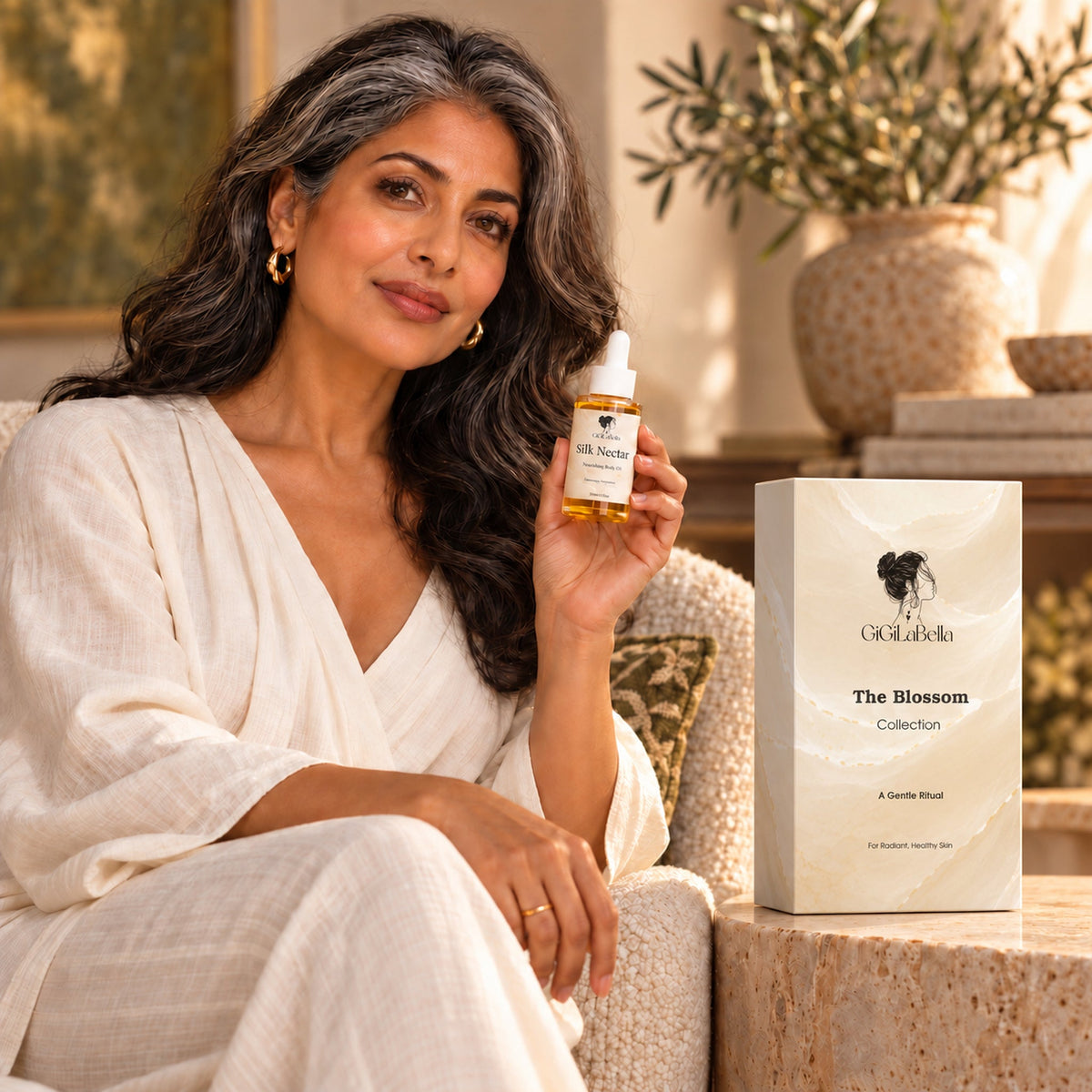 Mature model holding Silk Nectar nourishing facial oil beside The Blossom Collection gift box